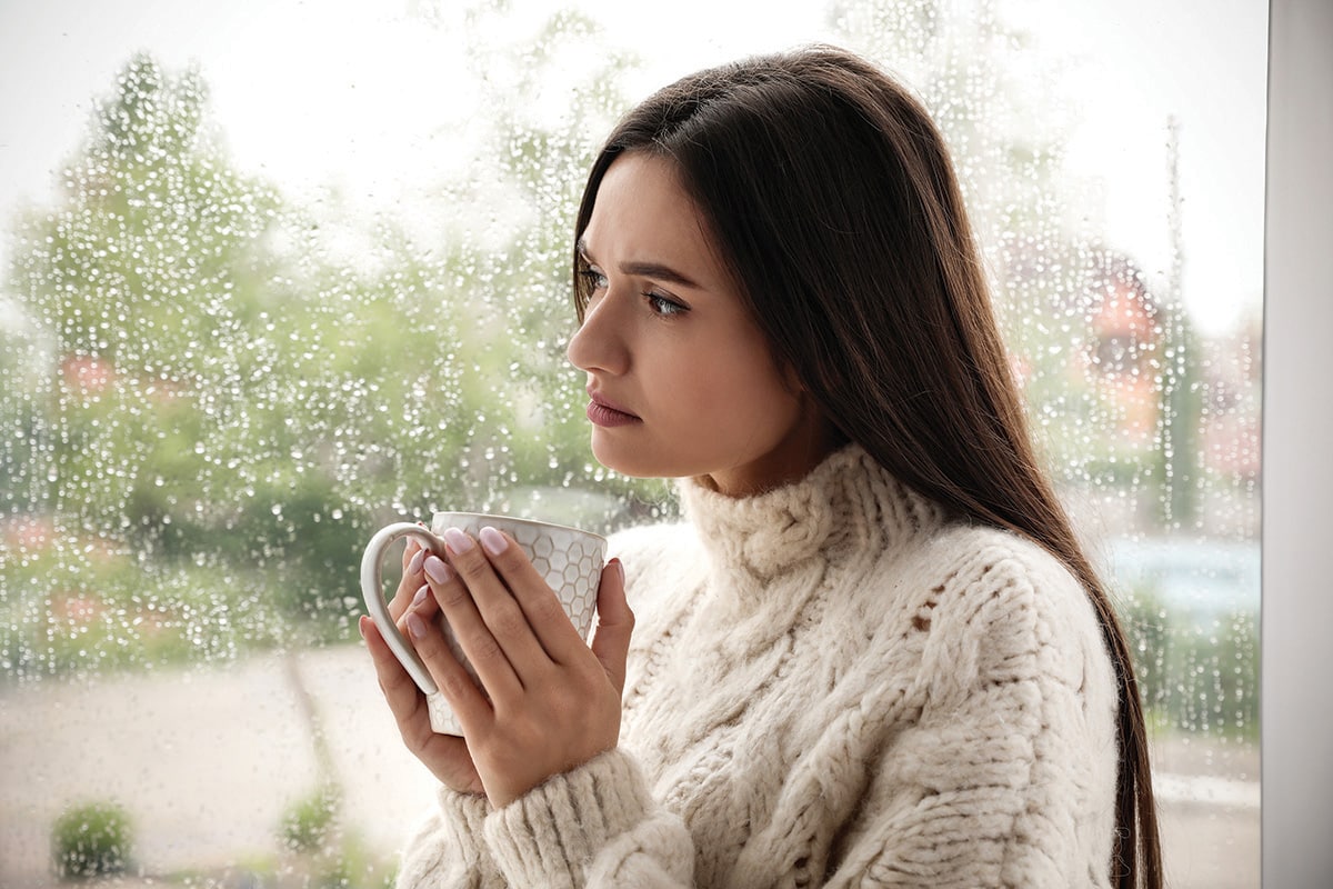 Sad Beautiful Woman With Cup Near Window Indoors On Rainy Day